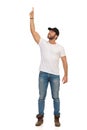 Young Man In Jeans, White T-shirt And Black Cap Is Standing With Arm Raised And Pointing Up Royalty Free Stock Photo