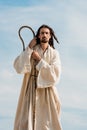 Man in jesus robe holding wooden cane against blue sky