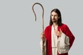 Man in jesus robe holding wooden cane while putting hand on chest isolated on grey
