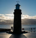 A man jogs around a lighthouse with him and the lighthouse is harp silhouette Royalty Free Stock Photo