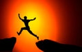 Man jumping across the gap from one rock to cling to the other. Man jumping over rocks with gap on sunset fiery background. Royalty Free Stock Photo