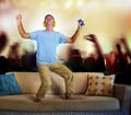 Man jumping on sofa couch listening to music with mobile phone and headphones imagine as famous rock band concert and fans audienc Royalty Free Stock Photo