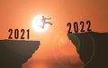 Man Jumping from 2021 to 2022 Over Cliff . happy new year 2022. Sunset background Young guy Jumps between two Cliffs or two years Royalty Free Stock Photo