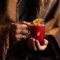 Man keeps warm holds cup of hot mulled wine while wrapped in blanket, close up shot. Alcoholic drink. Male hands holding