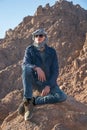 Man in a keffiyeh sitting on a rock in the desert