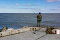 Man in khaki clothes is fishing on the concrete shore of a cold sea in Baltiysk