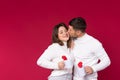 A man kisses on the cheek a smiling woman on a red background. White cups for tea and lovers& x27; time Royalty Free Stock Photo