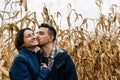 A man kisses a happy woman on the cheek while walking outside the city in a cornfield in autumn