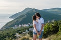 Man kisses a woman on the cheek and hugs, standing on a mountain with seascape. Side view.