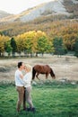 Man kisses woman on the forehead on a green lawn next to a grazing horse Royalty Free Stock Photo
