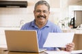 Man in kitchen with laptop and paperwork smiling Royalty Free Stock Photo