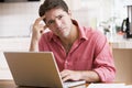 Man in kitchen using laptop frowning Royalty Free Stock Photo