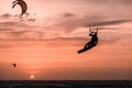 Man kitesurfer athlete jumping at sunset, silhouette at dusk man doing board grab on orange background