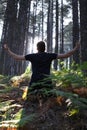 Man Kneeling with Arms Lifted in Forest