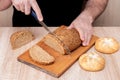 A man with a knife cuts bread on a wooden board. French baguettes. Different breeds on wooden background