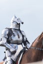 A man knight with half opened helmet riding a brown horse holding a sword