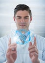 Man in lab coat holding up glass device with blue medical interface and flare against grey backgroun