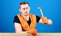 Man, labourer, handyman in bright vest and protective gloves handcrafting, blue background. Handcrafting concept