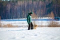 A man with a labrador retriever dog walking across a snowy field