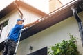 Man on ladder cleaning house gutter