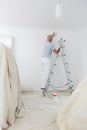 Man On Ladder Decorating Domestic Room With Paint Brush