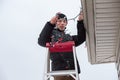 Man climbing a ladder to hang christmas lights outdoors.