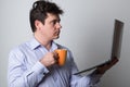 Man with a laptop is drinking morning tea. Young man works remotely on a laptop and drinks
