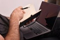 A man with a laptop on his lap taking notes in a notebook, close-up, online business analysis