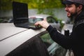 Man with a laptop in parking lot in yard near car is doing manipulations with cyber system, concept. Royalty Free Stock Photo