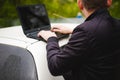 Man with a laptop in parking lot in yard near car is doing manipulations with cyber system, concept. Royalty Free Stock Photo