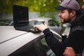 Man with a laptop in parking lot in yard near car is doing manipulations with cyber system, concept. Royalty Free Stock Photo