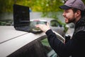 Man with a laptop in parking lot in yard near car is doing manipulations with cyber system, concept. Royalty Free Stock Photo