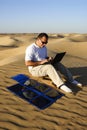 Man with a laptop and a portable folding solar kit charger in the midst of desert sand dunes Royalty Free Stock Photo
