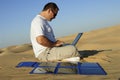 Man with Laptop and Portable Solar Charger in Desert Dunes, Renewable Energy Concept