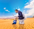 Man with laptop sitting on toilet bowl in desert Royalty Free Stock Photo