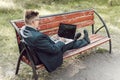 Man with laptop at summer park on bright day. businessman sitting on bench and watching on the laptop in city park Royalty Free Stock Photo