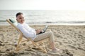 Man with laptop working on the beach sitting on a deckchair Royalty Free Stock Photo