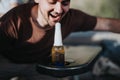 Man laughing and leaning towards an unopened beer bottle on a table