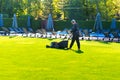 A man with a lawn mower mows grass on the lawn at a country club by the pool. Royalty Free Stock Photo