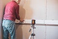 A man lays ceramic tiles on tile adhesive on a wall using a laser level. Home renovation, tile installation in the Royalty Free Stock Photo