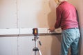 A man lays ceramic tiles on tile adhesive on a wall using a laser level. Home renovation, tile installation in the Royalty Free Stock Photo