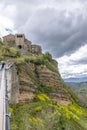 A man leans over the bridge to photograph the dying city, Civita di Bagnoregio, Italy, under a dramatic sky