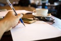 Man left handed writing in note with pen on paper with cell phone and coffee cup Royalty Free Stock Photo