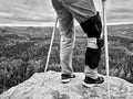 Man with leg in knee cages and crutches for stabilization stay on rock. Hurt tourist walk in mountains