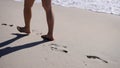 Male legs walking along sea coastline. Man spending summer holiday at seaside leaving footprints at wet sand beach Royalty Free Stock Photo