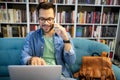 Man in library talking on cell phone and working on laptop Royalty Free Stock Photo