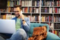 Man in library talking on cell phone and working on laptop Royalty Free Stock Photo