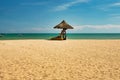 A man lifeguard, sitting under an umbrella of palm leaves on a deserted beach of Hainan Island. Royalty Free Stock Photo