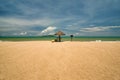 A man lifeguard, sitting under an umbrella of palm leaves on a deserted beach of Hainan Island. Royalty Free Stock Photo