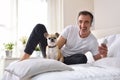 Smiling man listening music lying in bed with chihuahua